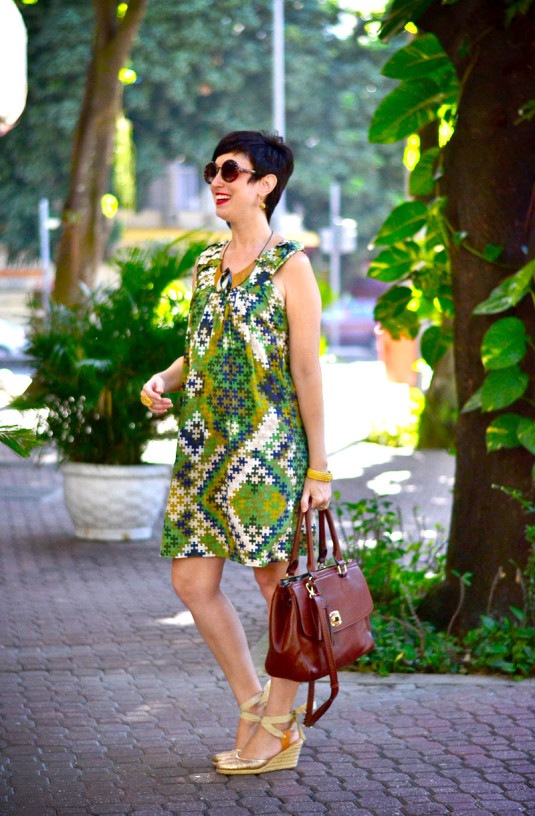 vestido curto com estampa de quebra-cabeça nas cores verde, azul, verde claro e branco, colar de madeira, sandália dourada