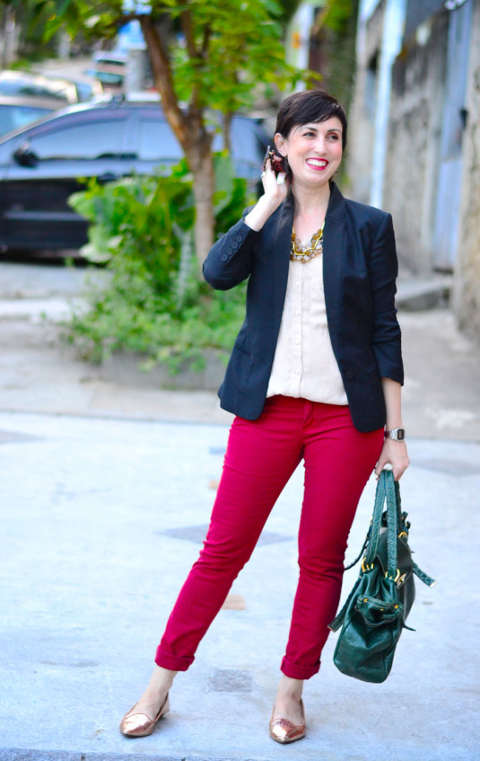 camisa sem mangas creme na frente e preta atrás, blazer preto, calça vermelho escuro, sapatilha de bico fino dourada, bolsa de couro verde, colar de murano dourado e bronze