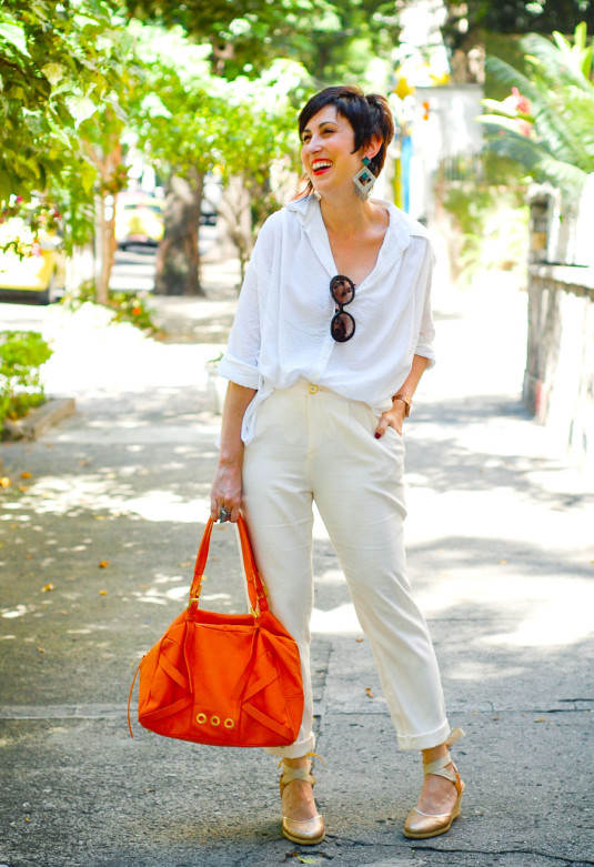 camisa branca de algodão soltinha e com textura, calça de cintura alta creme, espadrilhe de salto com dourado de gliter, bolsa laranja, brinco grande em forma de losango prata com detalhes em verde e franjas prata