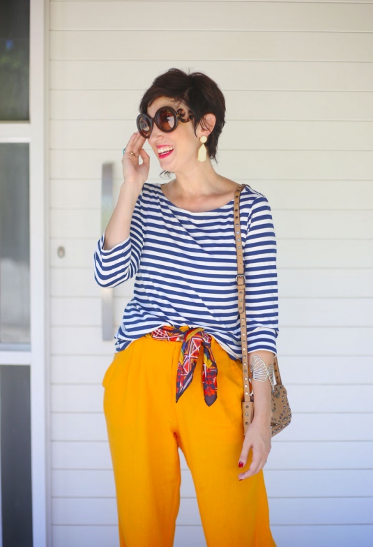 blusa de manga 3/4 listrada azul marinho, lenço na cintura vermelho, azul e amarelo, pantalona mostarda de linho, sandálias espadrilhes douradas, bolsa pequena em tom cru