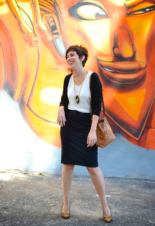 cardigan preto, blusa de viscose sem mangas offwhite, saia lápis preta, scarpin de oncinha com taxas, bolsa saco marrom claro, colar pendurado com pingente dourado e preto e branco