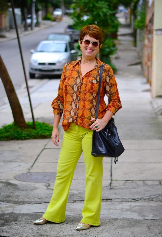 camisa com estampa de detalhes de couro de cobra em laranja e amarleo claro, calça flare verde limão, sapatilha bico fino dourada, bolsa saco preta