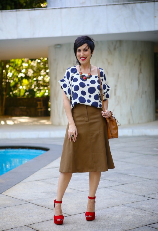 saia midi de cintura alta meio rodada bem feminina cor burro quando foge, sandália meia pata salto altíssimo vermelha de camurça, blusa de manga curta de bolas grandes azuis, colar com 4 bolas em pedras e ferragens vermelhas e beges, bolsa saco caramelo