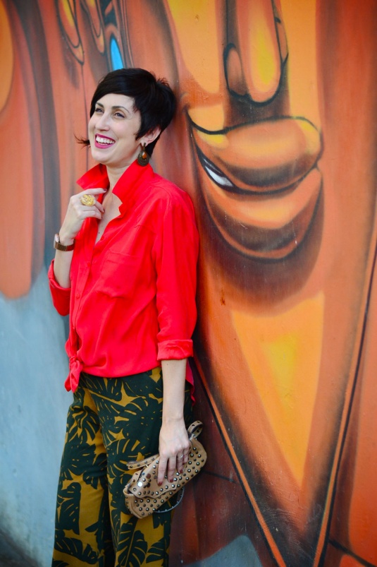 camisa vermelha de seda, calça pantalona curta caramelo com estampas de flores costela de adão em verde escuro, sandália de salto em tiras de couro nobuck caramelo, bolsa pequena de mão bege com tachas pratas