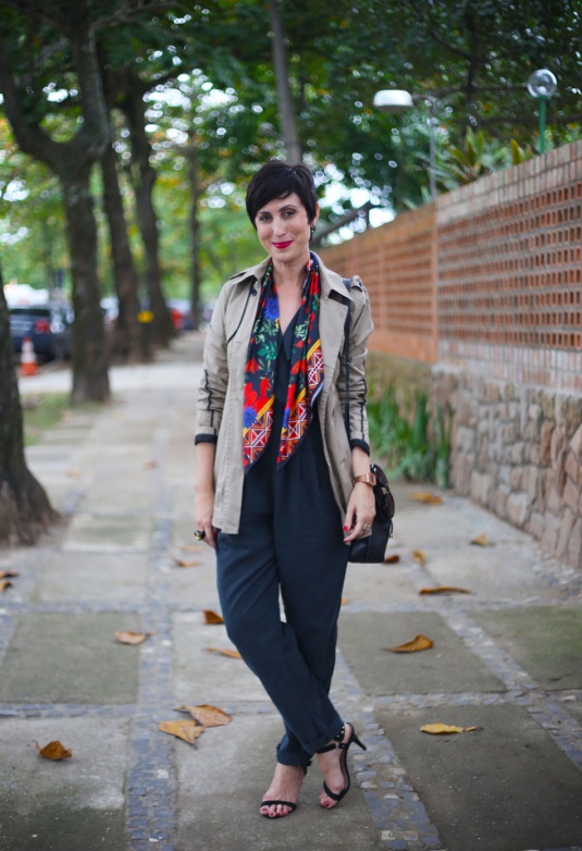macacão preto com lenço colorido estampado de vermelho, azul e laranja ao longo dele, trench coat curto cáqui e sandália preta de duas tiras