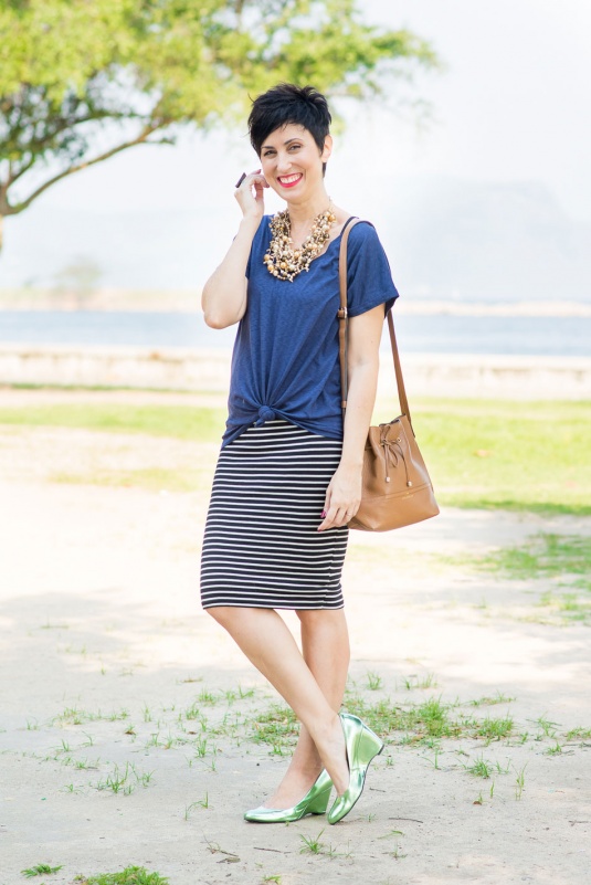 t-shirt azul escura com saia lápis de malha listrada pb, scarpin de salto anabela verde metalizado, bolsa saco caramelo, maxi colar de diferentes bolinhas douradas