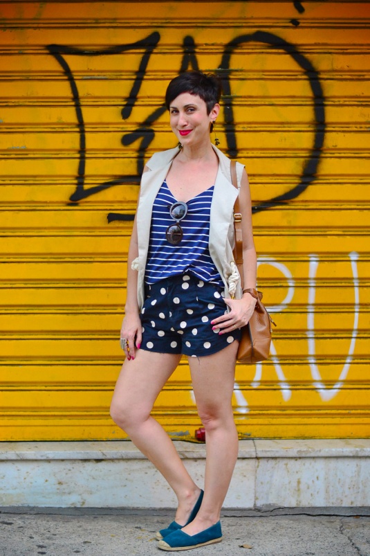 short curto azul marinho de bolotas brancas, regata listrada azul e branco, maxi colete em tom cru, alpargatas azuis, bolsa saco caramelo
